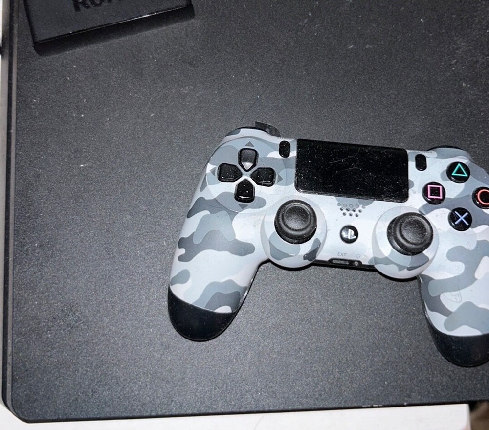 black ps4 console with a grey and black controller. + a black charging port.